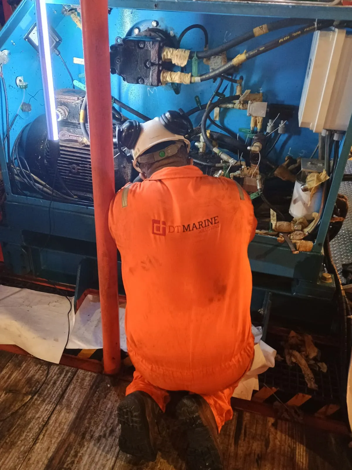 Técnico da DT Marine ajoelhado trabalha em uma unidade azul com motor, bombas e mangueiras hidráulicas