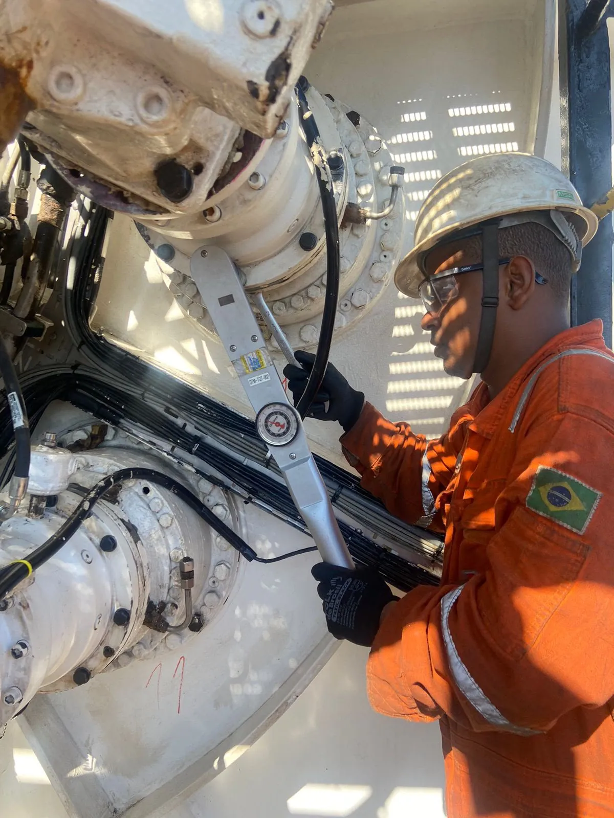 Técnico de macacão laranja e capacete usa um torquímetro de relógio para apertar os parafusos de um flange em um equipamento